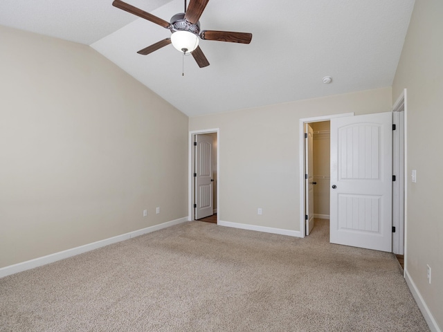 unfurnished bedroom featuring a walk in closet, vaulted ceiling, light carpet, a closet, and ceiling fan