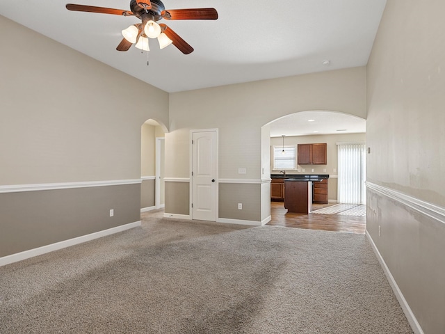 unfurnished living room with ceiling fan, light colored carpet, and sink