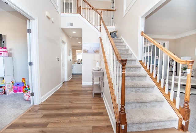 stairs featuring hardwood / wood-style flooring, crown molding, and a towering ceiling