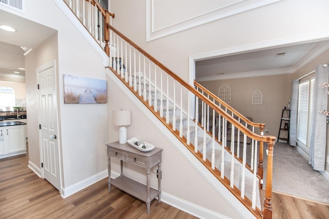 staircase with crown molding, sink, a healthy amount of sunlight, and hardwood / wood-style floors