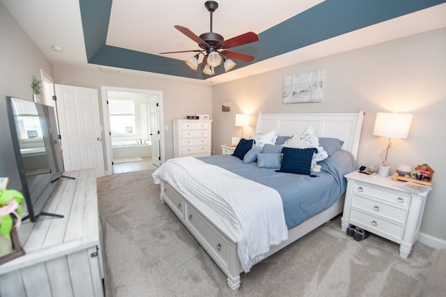 carpeted bedroom featuring a raised ceiling, ceiling fan, and ensuite bathroom