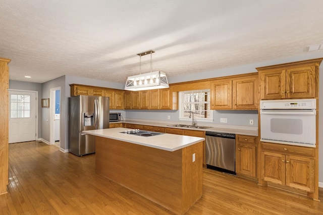 kitchen with a kitchen island, decorative light fixtures, sink, light hardwood / wood-style floors, and stainless steel appliances