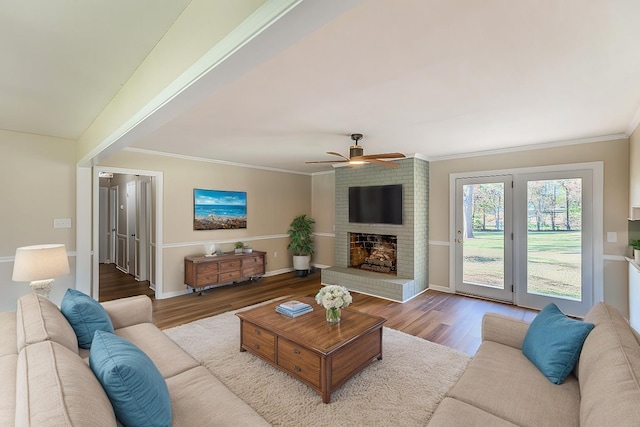 living room featuring a brick fireplace, crown molding, wood-type flooring, and ceiling fan