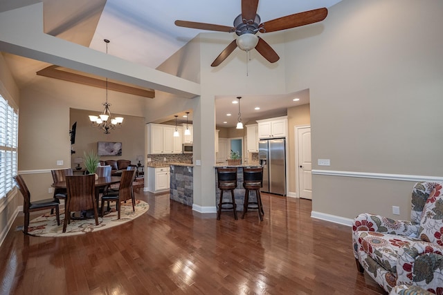 dining room with ceiling fan with notable chandelier, dark hardwood / wood-style floors, and high vaulted ceiling