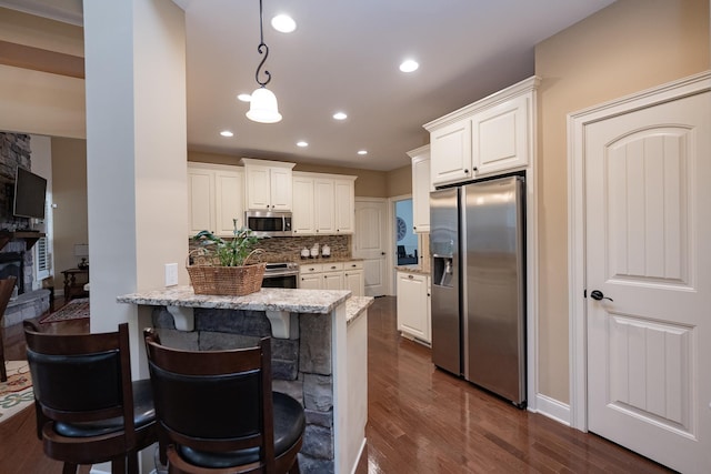 kitchen featuring appliances with stainless steel finishes, white cabinetry, a kitchen bar, kitchen peninsula, and light stone countertops