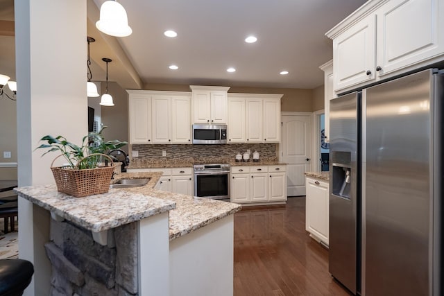 kitchen with sink, light stone counters, pendant lighting, stainless steel appliances, and white cabinets