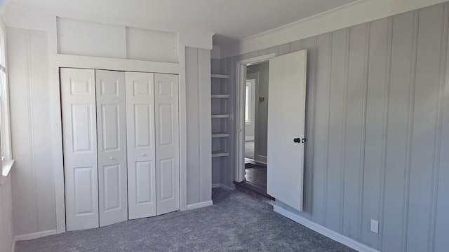 unfurnished bedroom with dark colored carpet, crown molding, and a closet