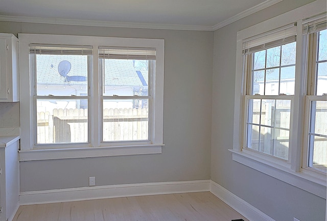 spare room featuring crown molding, a healthy amount of sunlight, and light wood-type flooring