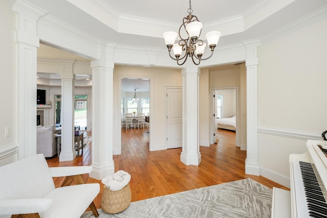 hall featuring a notable chandelier, a raised ceiling, and ornate columns