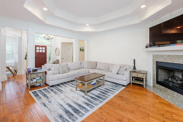 living room with decorative columns, ornamental molding, a notable chandelier, a raised ceiling, and light wood-type flooring