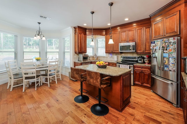 kitchen with crown molding, appliances with stainless steel finishes, hanging light fixtures, a center island, and light stone countertops