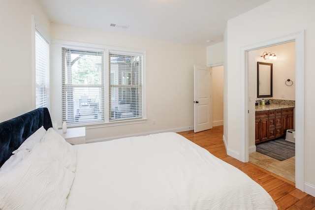 bedroom featuring connected bathroom, sink, and light hardwood / wood-style flooring