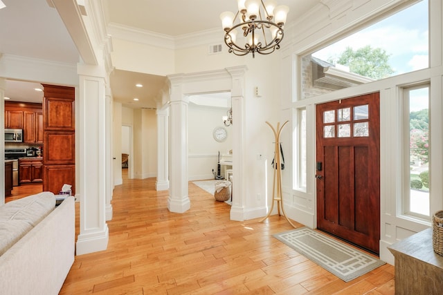 entryway featuring light wood-type flooring, ornamental molding, a chandelier, and ornate columns