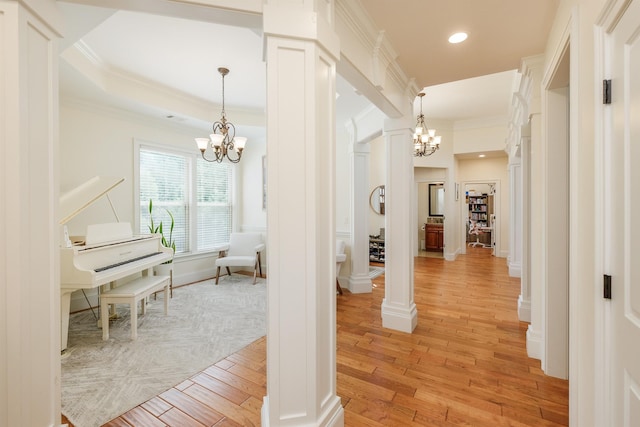 hallway with a notable chandelier, light hardwood / wood-style flooring, ornamental molding, and ornate columns