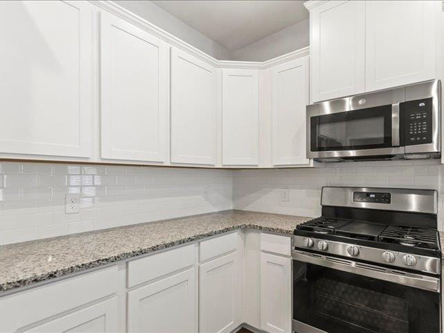 kitchen with backsplash, light stone countertops, white cabinets, and appliances with stainless steel finishes