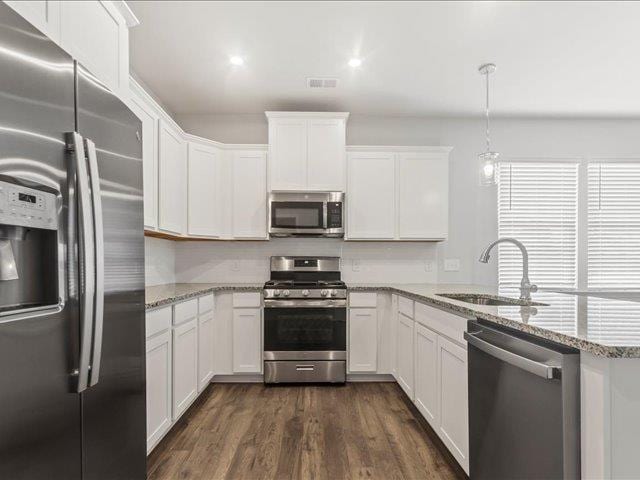 kitchen with sink, light stone counters, decorative light fixtures, stainless steel appliances, and white cabinets