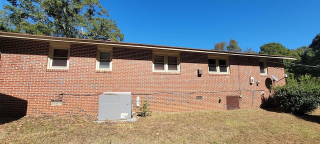 view of side of property featuring cooling unit, brick siding, and a yard