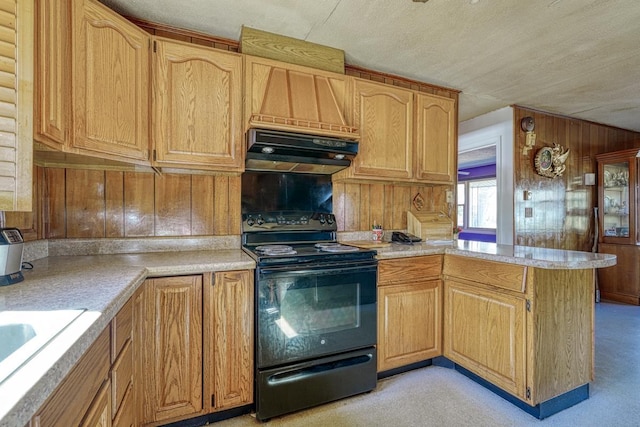kitchen with black electric range oven, light countertops, under cabinet range hood, wooden walls, and a peninsula