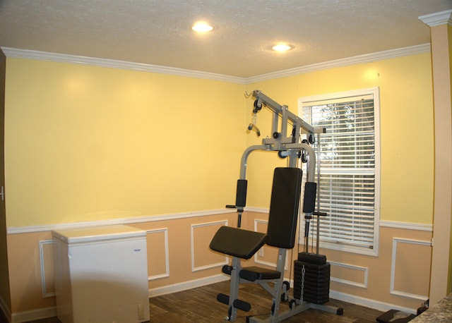 exercise area with ornamental molding, dark wood-type flooring, and a textured ceiling