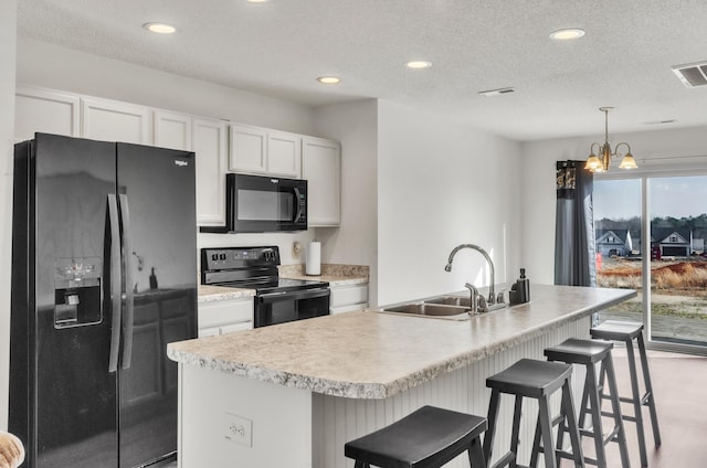 kitchen featuring a kitchen island with sink, sink, white cabinets, and black appliances