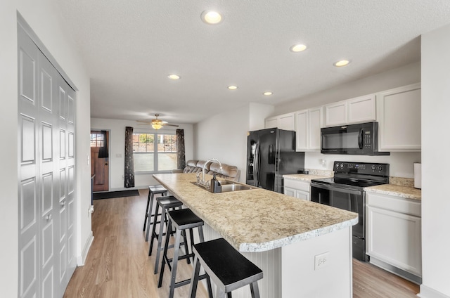 kitchen featuring a kitchen island with sink, sink, a breakfast bar, and black appliances