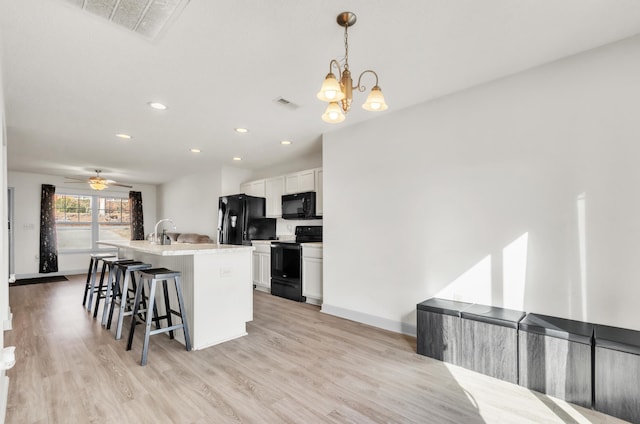 kitchen with white cabinetry, a kitchen breakfast bar, hanging light fixtures, black appliances, and a center island with sink