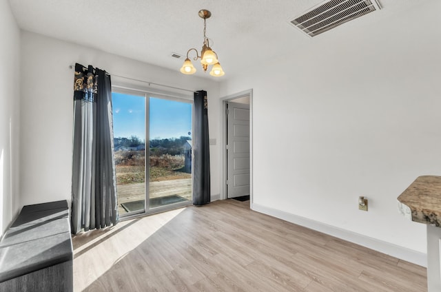 unfurnished room featuring a textured ceiling, an inviting chandelier, and light hardwood / wood-style flooring