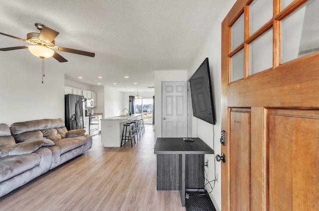 living room with ceiling fan, a textured ceiling, and light wood-type flooring