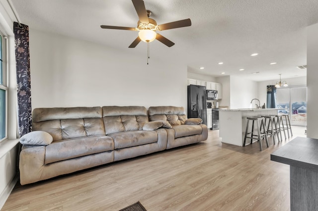 living room with ceiling fan, light hardwood / wood-style flooring, and a textured ceiling