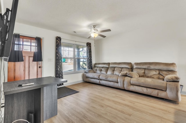 living room with ceiling fan, a textured ceiling, and light wood-type flooring