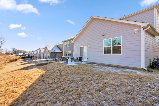 back of property with a yard, a patio area, and a trampoline