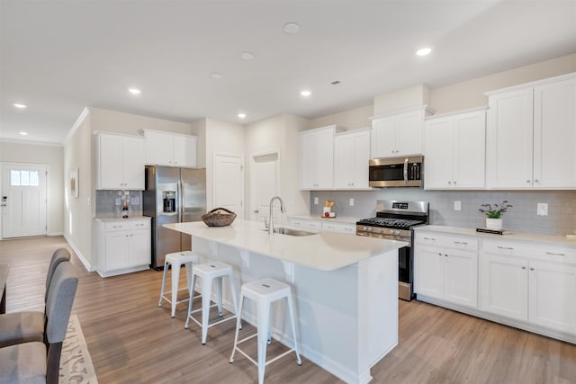 kitchen with appliances with stainless steel finishes, a kitchen island with sink, sink, and white cabinets