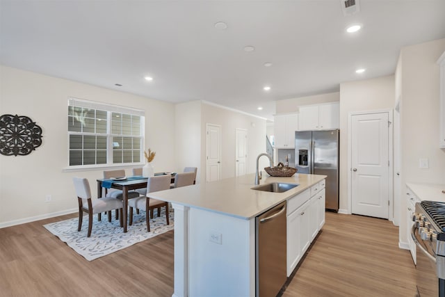 kitchen featuring sink, appliances with stainless steel finishes, white cabinetry, a center island with sink, and light wood-type flooring