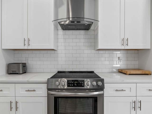 kitchen with white cabinetry, light stone counters, island range hood, and stainless steel electric range