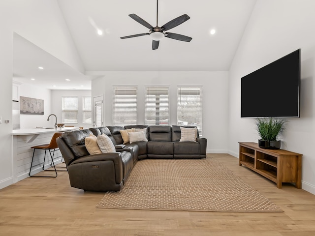 living room with ceiling fan, high vaulted ceiling, sink, and light wood-type flooring