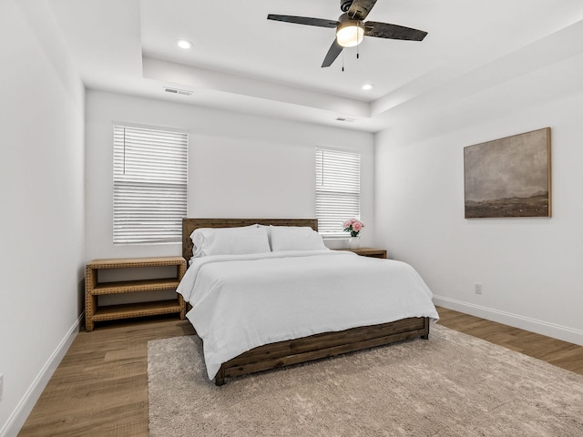 bedroom with ceiling fan, wood-type flooring, and a raised ceiling