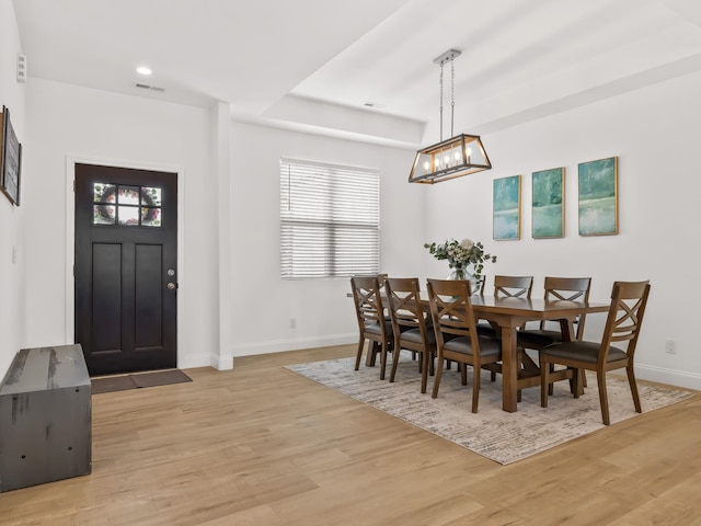 dining area featuring a raised ceiling, light hardwood / wood-style flooring, and a wealth of natural light