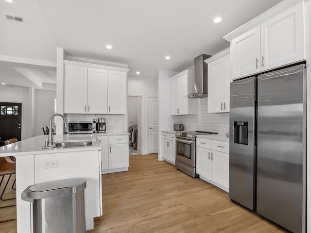 kitchen with sink, white cabinets, stainless steel appliances, light wood-type flooring, and wall chimney exhaust hood