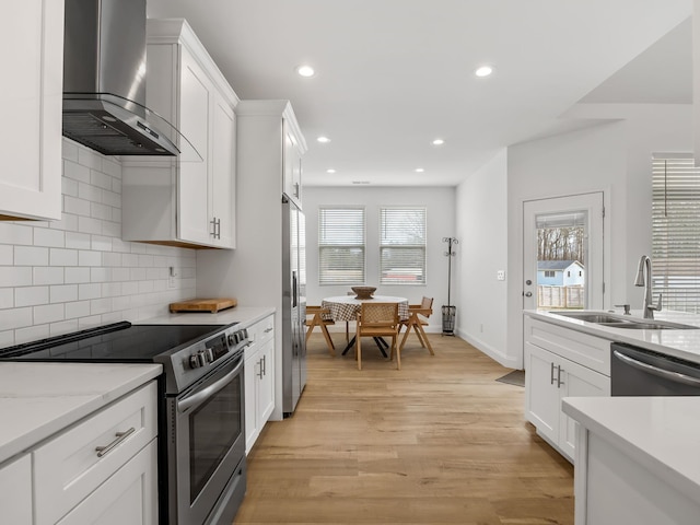 kitchen with sink, white cabinetry, stainless steel appliances, wall chimney exhaust hood, and light wood-type flooring