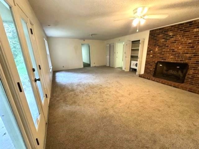 unfurnished living room featuring a fireplace, carpet floors, a textured ceiling, and ceiling fan