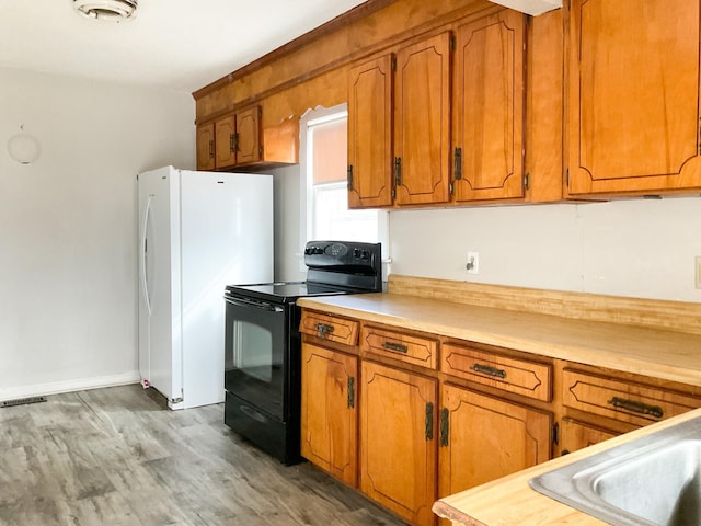 kitchen with white refrigerator, black range with electric stovetop, and hardwood / wood-style floors