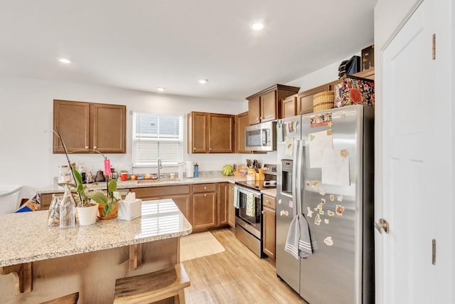 kitchen featuring a breakfast bar, sink, light stone counters, light wood-type flooring, and stainless steel appliances