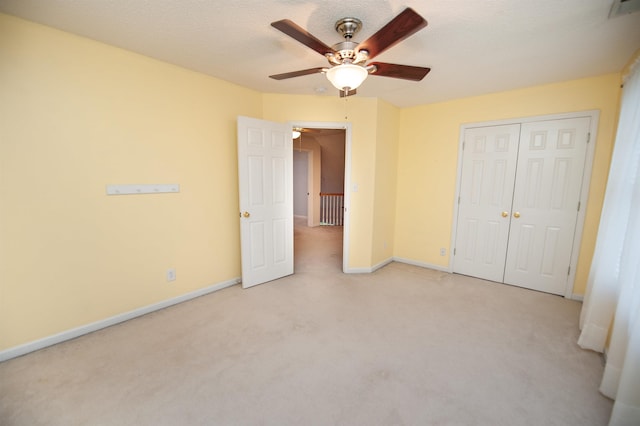 unfurnished bedroom with ceiling fan, light colored carpet, a closet, and a textured ceiling