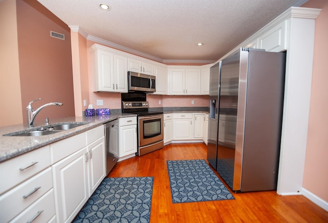 kitchen featuring sink, light hardwood / wood-style flooring, ornamental molding, stainless steel appliances, and white cabinets