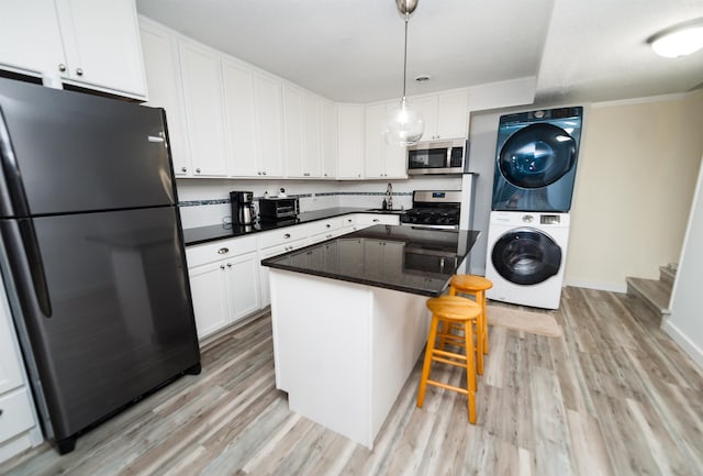 kitchen with pendant lighting, stainless steel appliances, stacked washer / dryer, and white cabinets