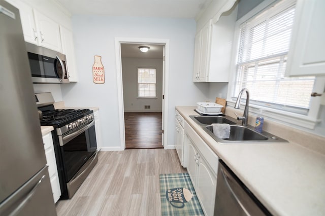 kitchen with appliances with stainless steel finishes, light hardwood / wood-style floors, sink, and white cabinets