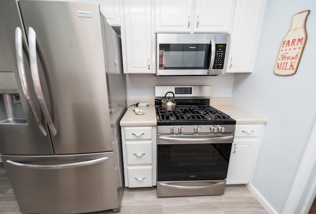 kitchen with stainless steel appliances, light hardwood / wood-style floors, and white cabinets