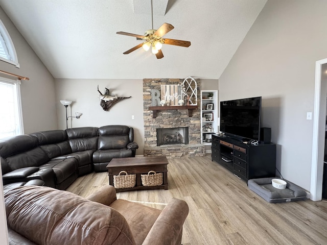 living room featuring ceiling fan, a fireplace, a textured ceiling, and light wood-type flooring