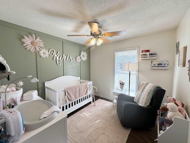 bedroom featuring hardwood / wood-style flooring, a textured ceiling, a nursery area, and ceiling fan