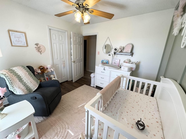 bedroom featuring a nursery area, hardwood / wood-style flooring, ceiling fan, a textured ceiling, and a closet